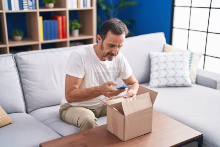 Foto de Hombre de mediana edad utilizando el teléfono inteligente desembalaje caja de cartón en casa - Imagen libre de derechos