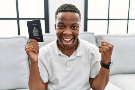 Foto de Young african man holding canada passport screaming proud, celebrating victory and success very excited with raised arms - Imagen libre de derechos