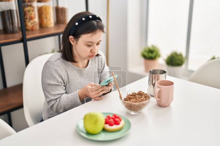 Photo for Young woman with down syndrome using smartphone having breakfast at home - Royalty Free Image