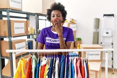 Foto de African young woman wearing volunteer t shirt at donations stand bored yawning tired covering mouth with hand. restless and sleepiness. - Imagen libre de derechos