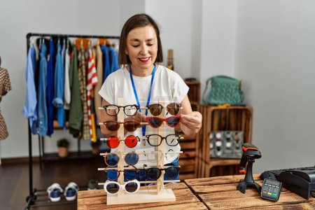 Foto de Mujer hispana de mediana edad trabajando vendiendo gafas de sol en tienda minorista - Imagen libre de derechos