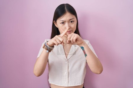 Foto de Chino joven mujer de pie sobre rosa fondo rechazo expresión cruzando dedos haciendo negativo signo - Imagen libre de derechos