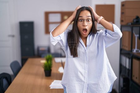 Photo for Young hispanic woman at the office crazy and scared with hands on head, afraid and surprised of shock with open mouth - Royalty Free Image