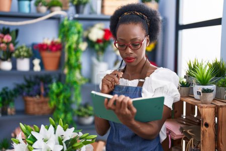 Foto de African american woman florist reading notebook with doubt expression at florist store - Imagen libre de derechos