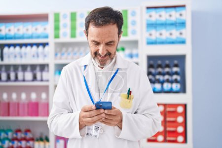 Téléchargez les photos : Homme moyen pharmacien utilisant smartphone travaillant à la pharmacie - en image libre de droit