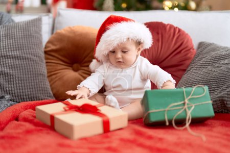 Photo for Adorable toddler wearing christmas hat sitting on sofa with present at home - Royalty Free Image