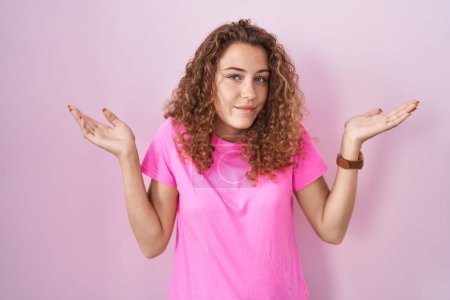 Photo for Young caucasian woman standing over pink background clueless and confused expression with arms and hands raised. doubt concept. - Royalty Free Image