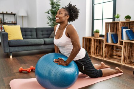 Téléchargez les photos : Afro-américaine femme entraînement abs exercice à l'aide de balle en forme à la maison - en image libre de droit