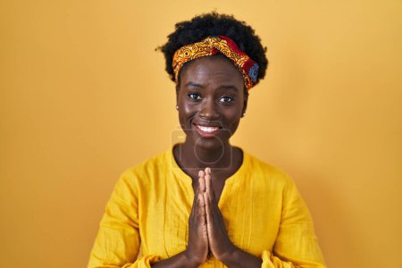Photo for African young woman wearing african turban praying with hands together asking for forgiveness smiling confident. - Royalty Free Image