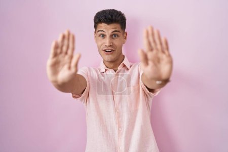 Téléchargez les photos : Young hispanic man standing over pink background doing stop gesture with hands palms, angry and frustration expression - en image libre de droit
