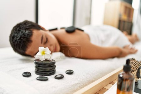 Photo for Young hispanic woman having back massage using black hot stones at beauty center - Royalty Free Image