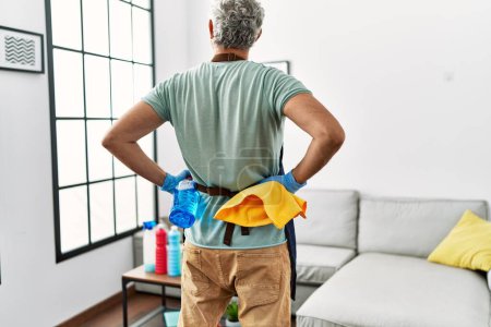 Photo for Middle age grey-haired man holding cloth and sprayer standing on back view at home - Royalty Free Image