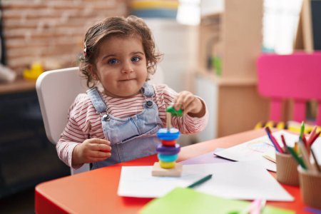 Téléchargez les photos : Adorable hispanique fille jouer avec cerceaux jeu assis sur la table à la maternelle - en image libre de droit