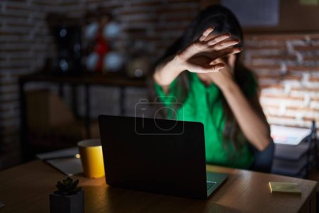 Foto de Young teenager girl working at the office at night covering eyes with hands and doing stop gesture with sad and fear expression. embarrassed and negative concept. - Imagen libre de derechos