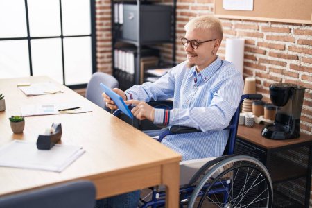 Foto de Joven hombre caucásico trabajador de negocios usando touchpad sentado en silla de ruedas en la oficina - Imagen libre de derechos