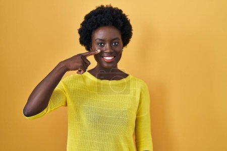 Téléchargez les photos : African young woman standing over yellow studio pointing with hand finger to face and nose, smiling cheerful. beauty concept - en image libre de droit