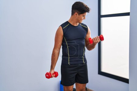 Photo for Young hispanic man smiling confident using dumbbells training at sport center - Royalty Free Image