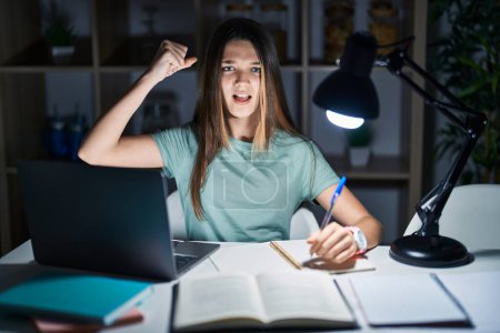Téléchargez les photos : Teenager girl doing homework at home late at night angry and mad raising fist frustrated and furious while shouting with anger. rage and aggressive concept. - en image libre de droit