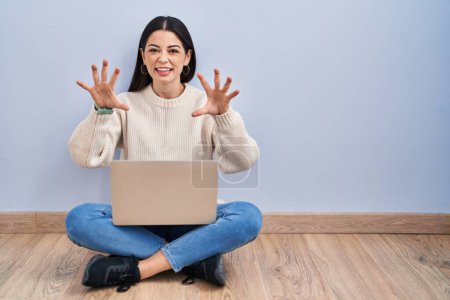 Téléchargez les photos : Jeune femme utilisant un ordinateur portable assis sur le sol à la maison souriant drôle faisant griffe geste comme chat, expression agressive et sexy - en image libre de droit