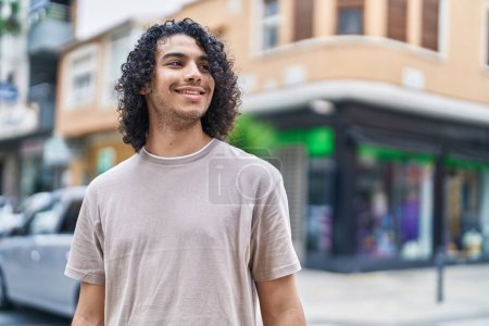 Téléchargez les photos : Jeune homme latino souriant confiant regardant du côté de la rue - en image libre de droit
