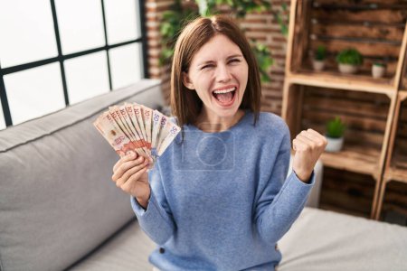 Photo for Young brunette woman holding colombian pesos screaming proud, celebrating victory and success very excited with raised arms - Royalty Free Image