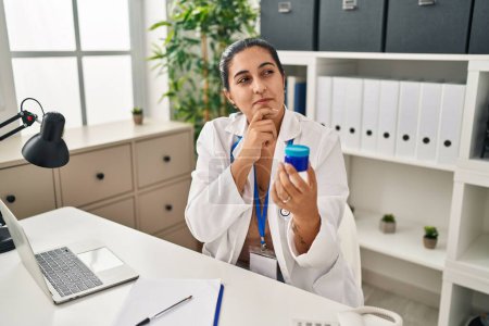 Photo for Young doctor hispanic woman holding serious face thinking about question with hand on chin, thoughtful about confusing idea - Royalty Free Image