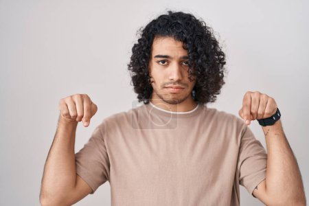 Photo for Hispanic man with curly hair standing over white background pointing down looking sad and upset, indicating direction with fingers, unhappy and depressed. - Royalty Free Image