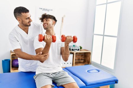 Photo for Two hispanic men physiotherapist and patient having rehab session using dumbbells at clinic - Royalty Free Image