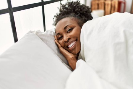 Foto de Mujer afroamericana sonriendo confiada acostada en la cama en el dormitorio - Imagen libre de derechos