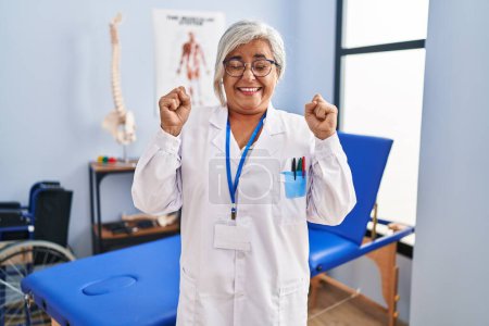 Photo for Middle age woman with grey hair working at pain recovery clinic excited for success with arms raised and eyes closed celebrating victory smiling. winner concept. - Royalty Free Image