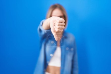 Téléchargez les photos : Jeune femme caucasienne debout sur fond bleu regardant malheureux et en colère montrant rejet et négatif avec les pouces vers le bas geste. mauvaise expression. - en image libre de droit