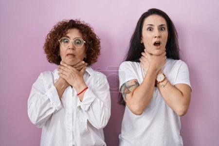 Photo for Hispanic mother and daughter wearing casual white t shirt over pink background shouting suffocate because painful strangle. health problem. asphyxiate and suicide concept. - Royalty Free Image
