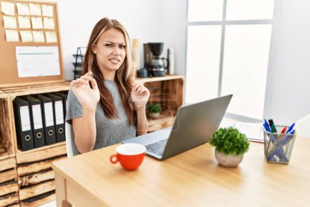 Photo for Young brunette woman working at the office with laptop disgusted expression, displeased and fearful doing disgust face because aversion reaction. with hands raised - Royalty Free Image