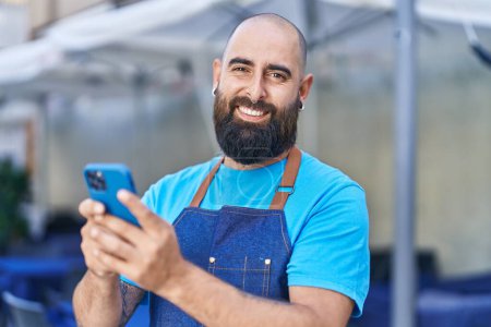 Photo for Young bald man waiter smiling confident using smartphone at coffee shop terrace - Royalty Free Image