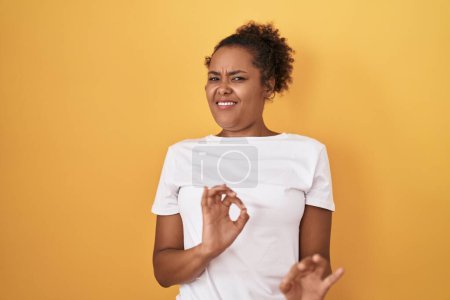 Téléchargez les photos : Young hispanic woman with curly hair standing over yellow background disgusted expression, displeased and fearful doing disgust face because aversion reaction. - en image libre de droit