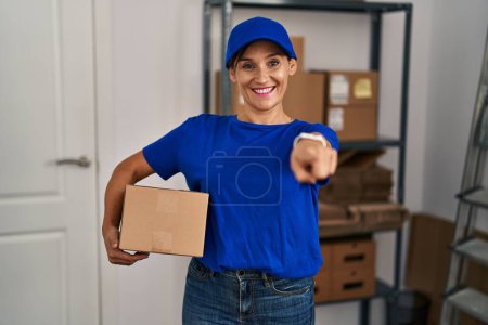 Foto de Middle age brunette woman working wearing delivery uniform and cap pointing to you and the camera with fingers, smiling positive and cheerful - Imagen libre de derechos