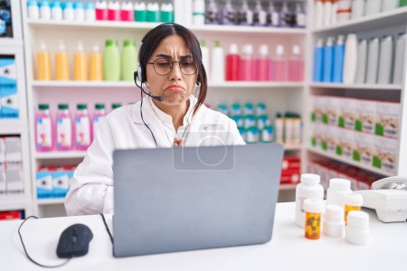 Photo for Young arab woman working at pharmacy drugstore using laptop begging and praying with hands together with hope expression on face very emotional and worried. begging. - Royalty Free Image