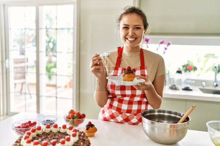 Photo for Young beautiful hispanic woman smiling confident eating cupcake at the kitchen - Royalty Free Image
