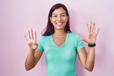 Photo for Young hispanic woman standing over pink background showing and pointing up with fingers number nine while smiling confident and happy. - Royalty Free Image