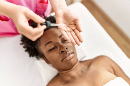 Foto de Mujer afroamericana acostada en mesa de masaje teniendo tratamiento facial en salón de belleza - Imagen libre de derechos