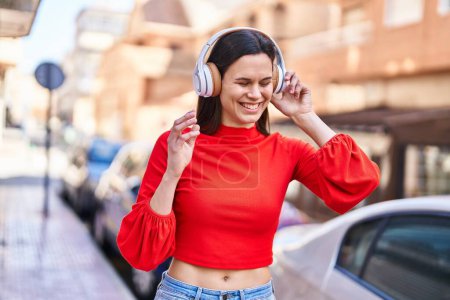 Foto de Joven hermosa mujer hispana sonriendo confiada escuchando música en la calle - Imagen libre de derechos
