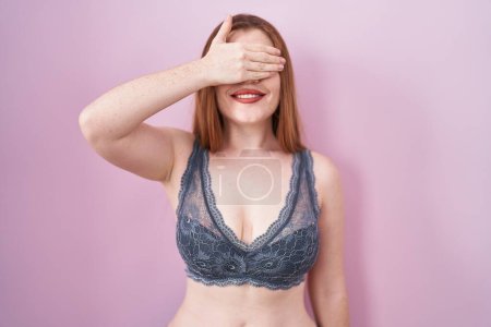 Téléchargez les photos : Redhead woman wearing lingerie over pink background smiling and laughing with hand on face covering eyes for surprise. blind concept. - en image libre de droit