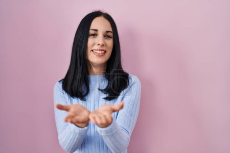 Photo for Hispanic woman standing over pink background smiling with hands palms together receiving or giving gesture. hold and protection - Royalty Free Image