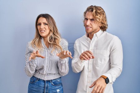 Photo for Young couple standing over blue background disgusted expression, displeased and fearful doing disgust face because aversion reaction. - Royalty Free Image