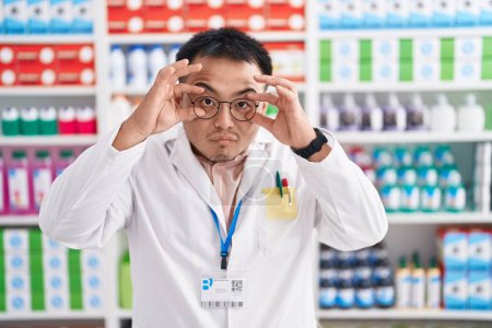 Foto de Joven chino trabajando en farmacia tratando de abrir los ojos con los dedos, soñoliento y cansado para la fatiga de la mañana - Imagen libre de derechos
