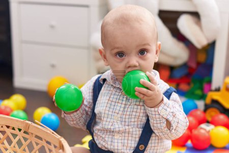 Téléchargez les photos : Adorable caucasien bébé sucer boule assis sur le sol à la maternelle - en image libre de droit