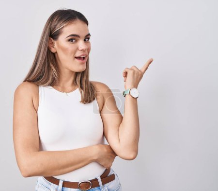 Photo for Hispanic young woman standing over white background with a big smile on face, pointing with hand finger to the side looking at the camera. - Royalty Free Image