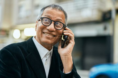 Téléchargez les photos : Moyen âge sud-est asiatique homme souriant parlant au téléphone à la ville - en image libre de droit