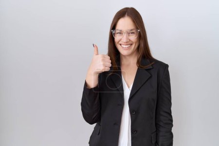 Photo for Beautiful brunette woman wearing business jacket and glasses doing happy thumbs up gesture with hand. approving expression looking at the camera showing success. - Royalty Free Image