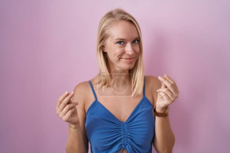 Photo for Young caucasian woman standing over pink background doing money gesture with hands, asking for salary payment, millionaire business - Royalty Free Image